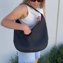 Woman holding a black shoulder bag against a light background