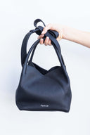 Black leather handbag with small silver Spixal logo held up by female hand on white background