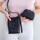 Person holding a black leather handbag and matching wallet, with a white background