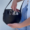 Person holding a black handbag with a white background, putting a phone in a phone pocket