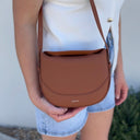 Person holding a tan crossbody bag with a neutral background