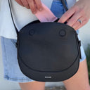 Person holding a black crossbody bag with a visible brand logo.