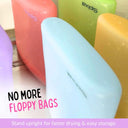 Five colourful Spixal silicone snack and sandwich bags in purple, red, light blue, green, and yellow, standing upright to show their shape and water-droplet finish as they sit to dry. Text overlays read 'NO MORE FLOPPY BAGS' and 'Stand upright for faster drying & easy storage '.