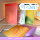 Five reusable silicone food sandwich and snack bags in red, blue, green, yellow and purple shown inside a refrigerator shelf, with text overlays reading 'FRIDGE & FREEZER FRIENDLY' and 'Perfect for meal prep & leftovers.'.